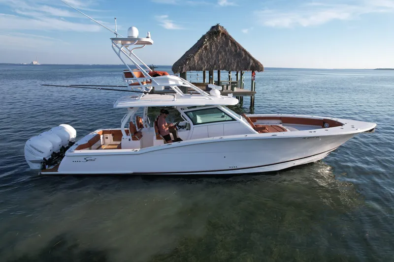 Slide: The Image of 2019 Scout 420 LXF boat on calm water near a thatched-roof dock. - 17