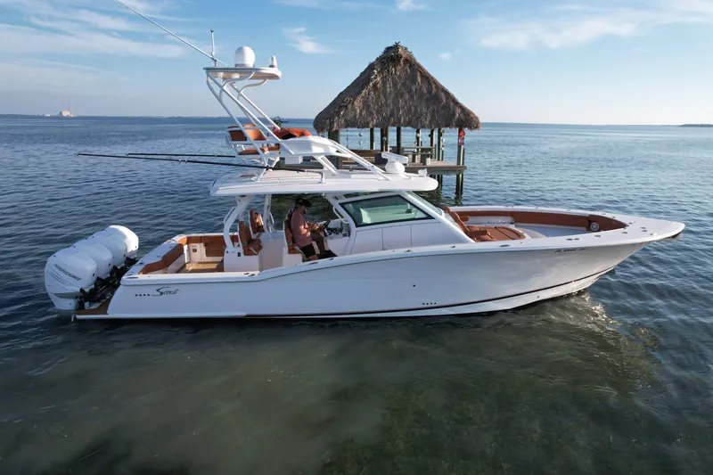 Slide: The Image of 2019 Scout 420 LXF boat cruising near a thatched-roof dock on calm waters. - 2