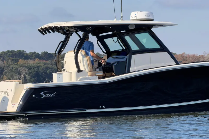 Slide: The Image of 2022 Scout 330 LXF boat cruising on a calm lake with a person at the helm. - 15