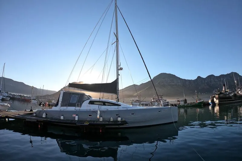 Slide: The Image of 2006 Maxim Yachts 57 sailboat docked in a serene marina with mountain backdrop. - 3