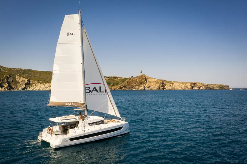 Slide: The Image of Sailing catamaran Bali 4.2, 2026 model, cruising near rocky coastline under clear blue sky. - 44