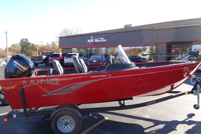 Slide: The Image of 2022 Lund 1650 Rebel XL SS boat in red, parked outside a marine dealership. - 15