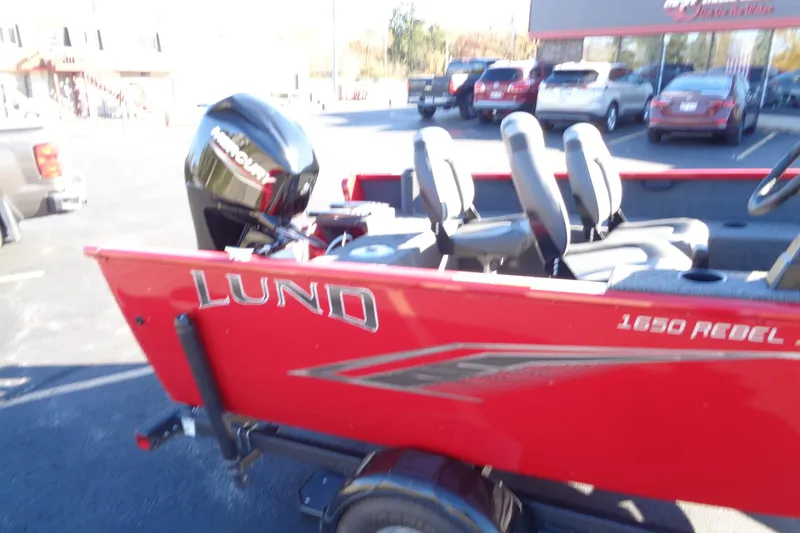 Slide: The Image of 2022 Lund 1650 Rebel XL SS boat in a parking lot, featuring a red exterior and Mercury engine. - 16