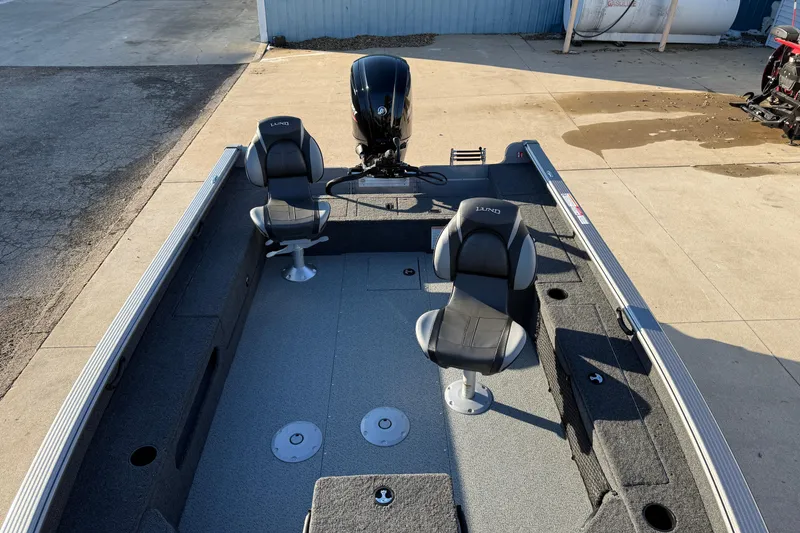 Slide: The Image of 2026 Lund 1875 Pro Guide boat interior with two seats and motor, parked on concrete. - 10
