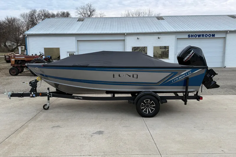 Slide: The Image of 2026 Lund 1775 Impact XS SS boat with cover, parked outside a showroom. - 29
