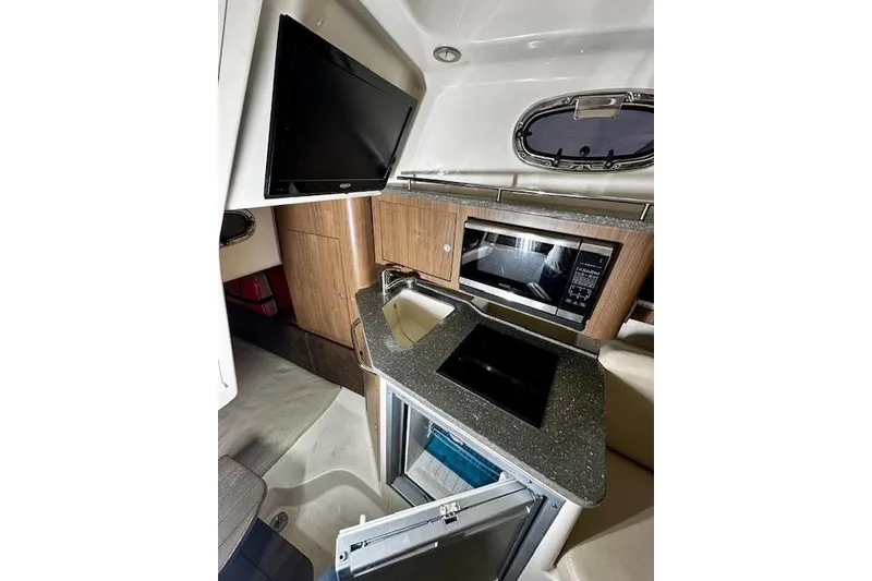 Slide: The Image of 2016 Boston Whaler 285 Conquest cabin with kitchenette, featuring a TV, microwave, and sink. - 16
