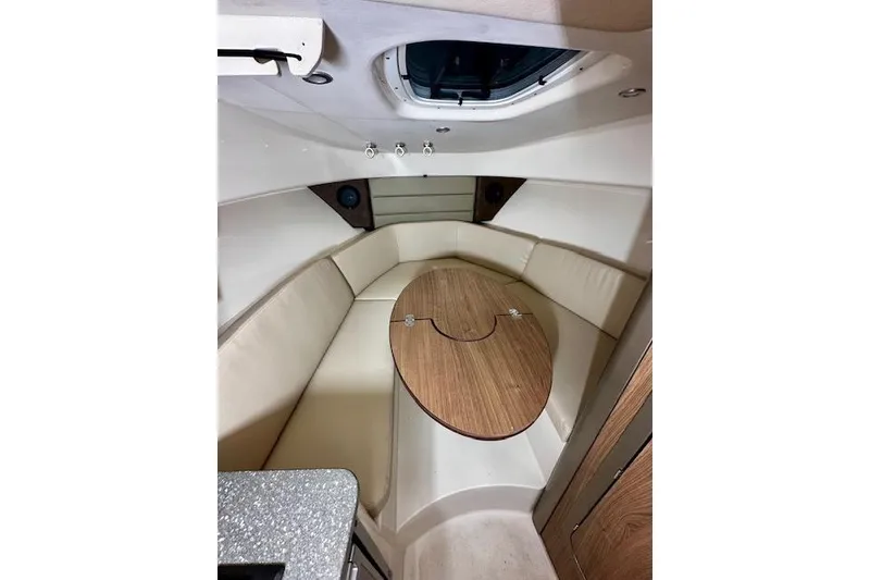 Slide: The Image of 2016 Boston Whaler 285 Conquest cabin interior with beige seating and wooden table. - 17
