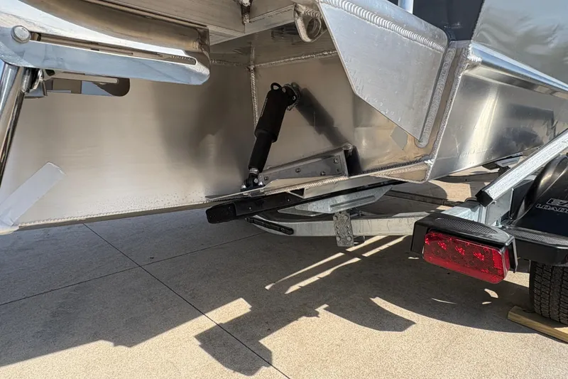 Slide: The Image of 2026 Lund 210 Heavy Gauge boat trailer detail with hydraulic components and rear light. - 10