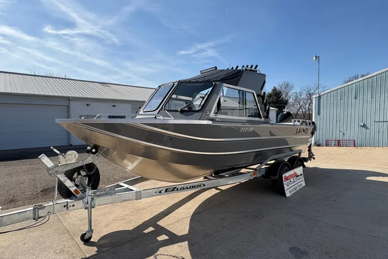 Slide: The Image of 2026 Lund 210 Heavy Gauge boat on trailer, parked outdoors under clear sky. - 17