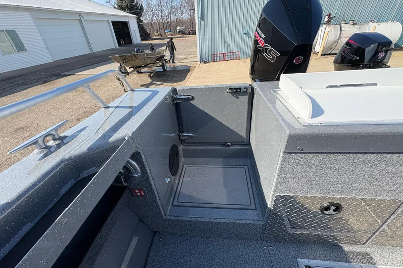 Slide: The Image of 2026 Lund 210 Heavy Gauge boat interior with motor, docked near a warehouse. - 47