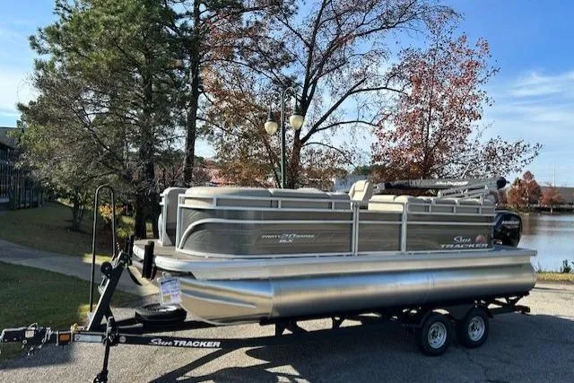 The Image of 2025 Sun Tracker Party Barge 20 DLX pontoon boat on trailer by a lake. - 0