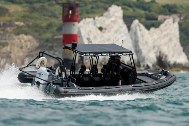 Slide: The Image of Manufacturer Provided Image: 2025 Highfield Patrol 860 boat cruising near a lighthouse and rocky cliffs. - 2