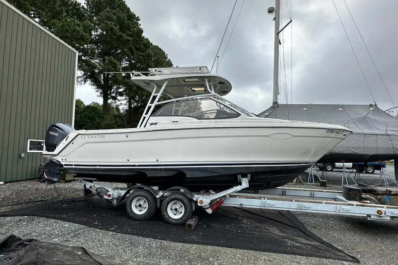 The Image of 2022 Cutwater C-24 DC boat on trailer, parked outdoors near trees and buildings. - 0