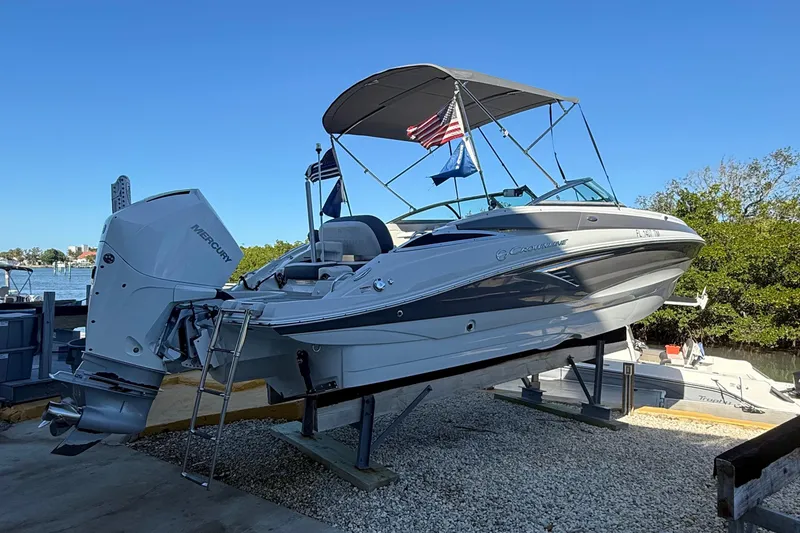 The Image of 2022 Crownline Eclipse E235 XS boat on a lift, with flags and Mercury engine. - 0
