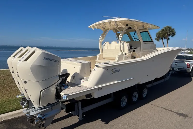 Slide: The Image of 2026 Scout 357 LXF boat with triple Mercury engines on a trailer by the water. - 3