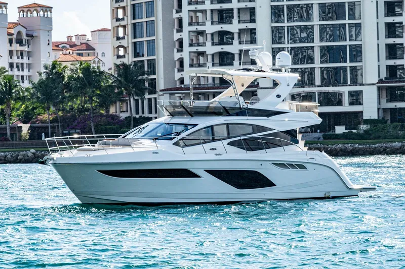 The Image of 2018 Sea Ray L550 Fly yacht cruising near luxury waterfront buildings. - 0