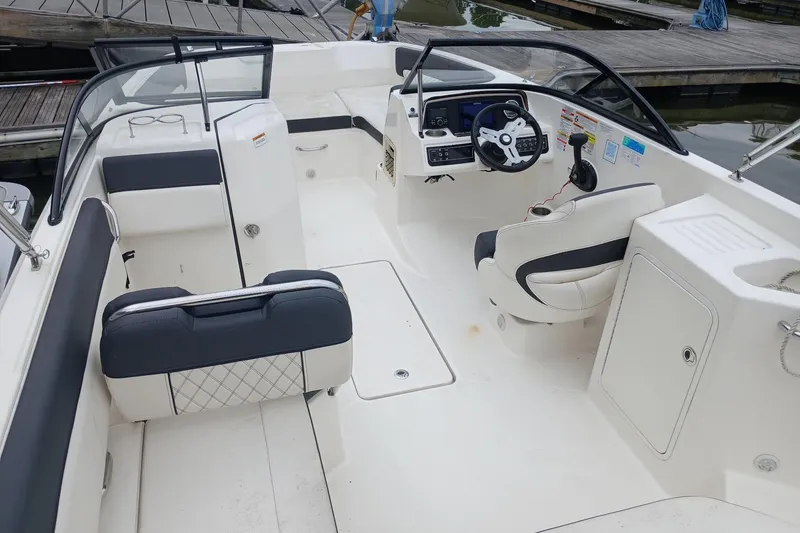 Slide: The Image of 2023 Bayliner DX 2200 boat interior with seating and steering console at dock. - 11