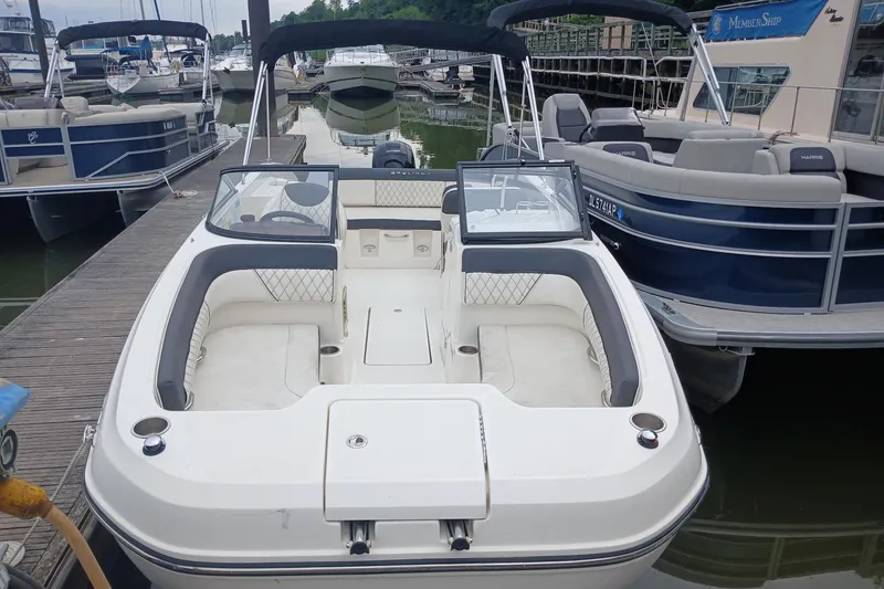 Slide: The Image of 2023 Bayliner DX 2200 boat docked at marina, featuring spacious seating and modern design. - 2