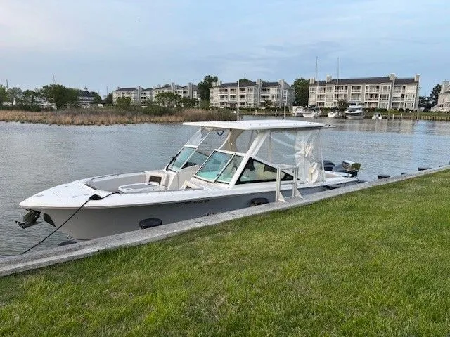 Slide: The Image of 2023 Sailfish 276DC boat docked by a grassy shore with buildings in the background. - 4