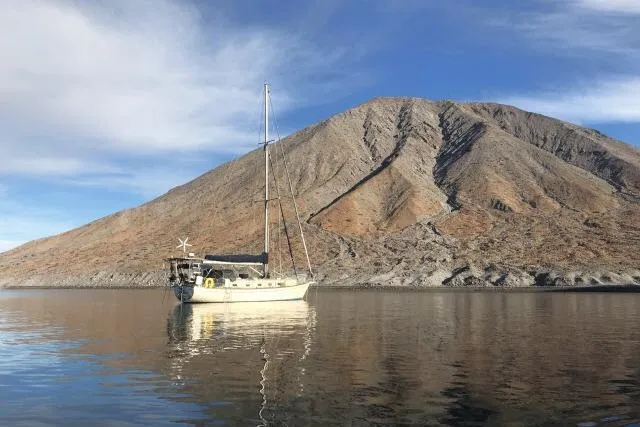 Slide: The Image of Sailboat Island Packet 45 (1999) anchored near a rocky mountain under a blue sky. - 61