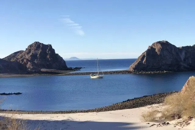 Slide: The Image of Sailboat anchored in a serene bay, surrounded by rocky cliffs and clear blue water. - 62