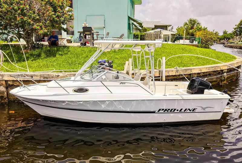 Slide: The Image of 1999 Pro-Line 201 Walkaround boat docked by a canal with lush greenery. - 2