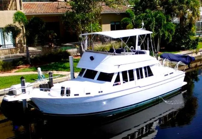 The Image of 2000 Mainship 430 Trawler docked by lush greenery and waterfront homes. - 0