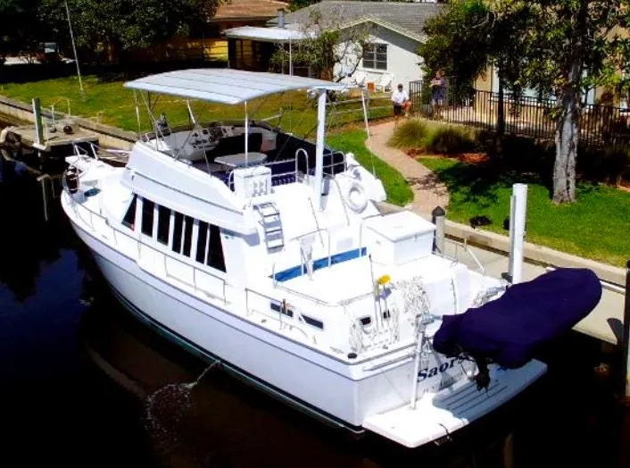 Slide: The Image of 2000 Mainship 430 Trawler docked near a residential area, featuring a spacious deck and canopy. - 2