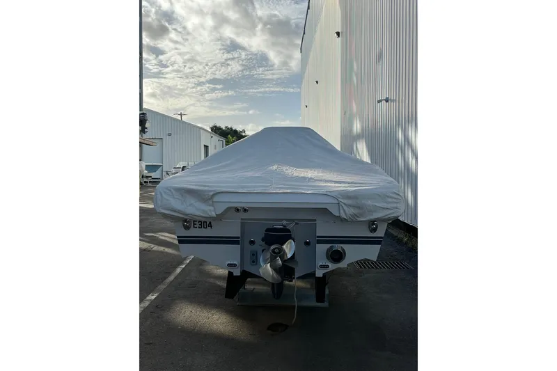 Slide: The Image of 2021 Novurania Chase 19 boat covered, parked beside a white building under a cloudy sky. - 11