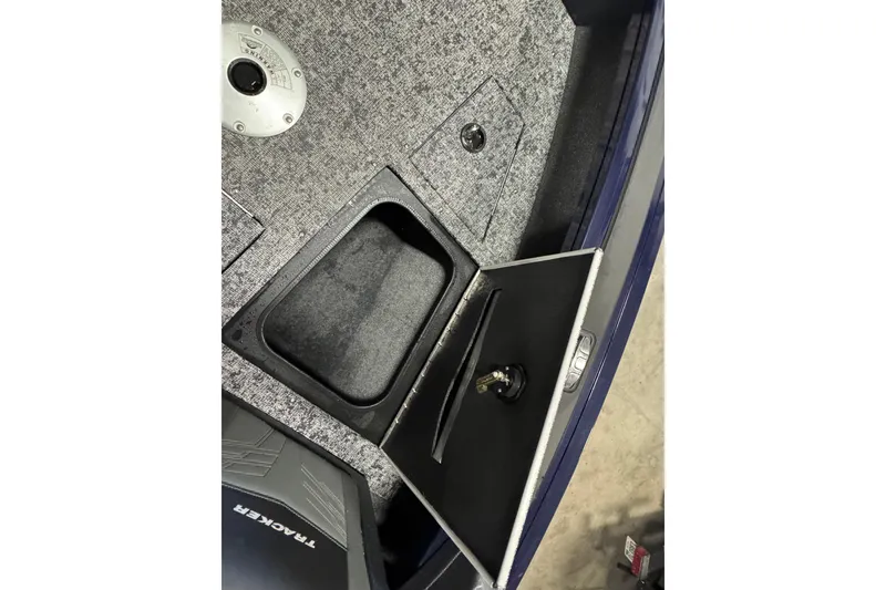 Slide: The Image of 2025 Tracker Targa V-19 WT boat storage compartment with open hatch and carpeted interior. - 23