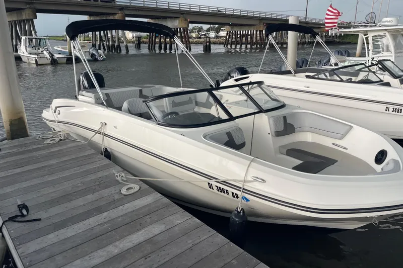 Slide: The Image of 2023 Bayliner VR6 Bowrider OB docked by a wooden pier, under a bridge. - 2