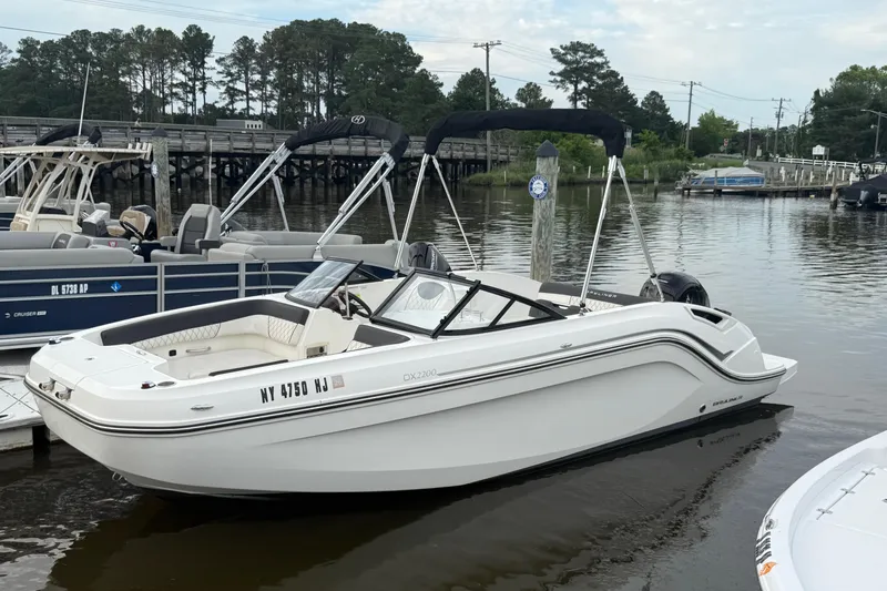 The Image of 2023 Bayliner DX 2200 boat docked on a calm river with trees in the background. - 0