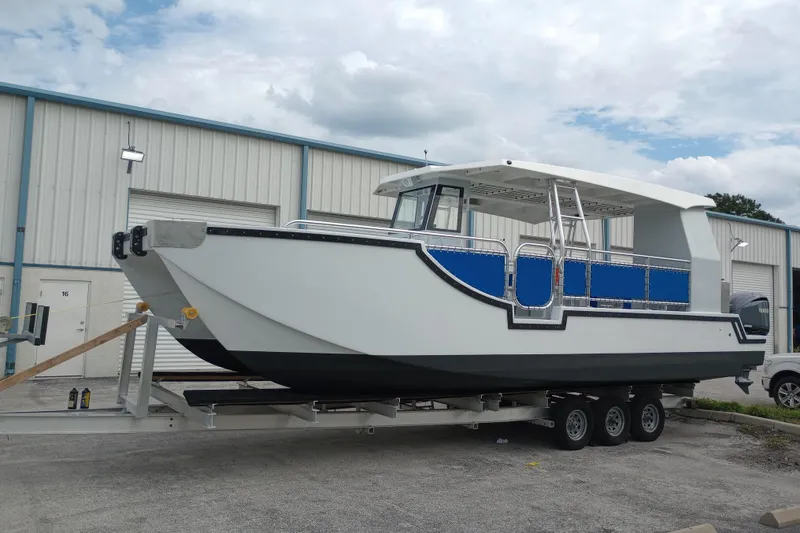 Slide: The Image of Custom Passenger Catamaran BYD34 2026 on trailer, parked outside industrial building. - 3