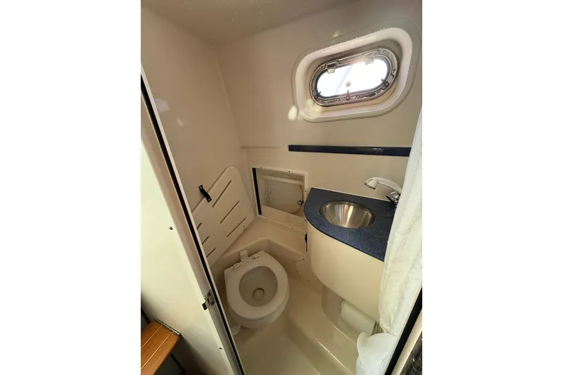 Slide: The Image of 2005 Pursuit 3070 Offshore boat bathroom with toilet, sink, and porthole window. - 15
