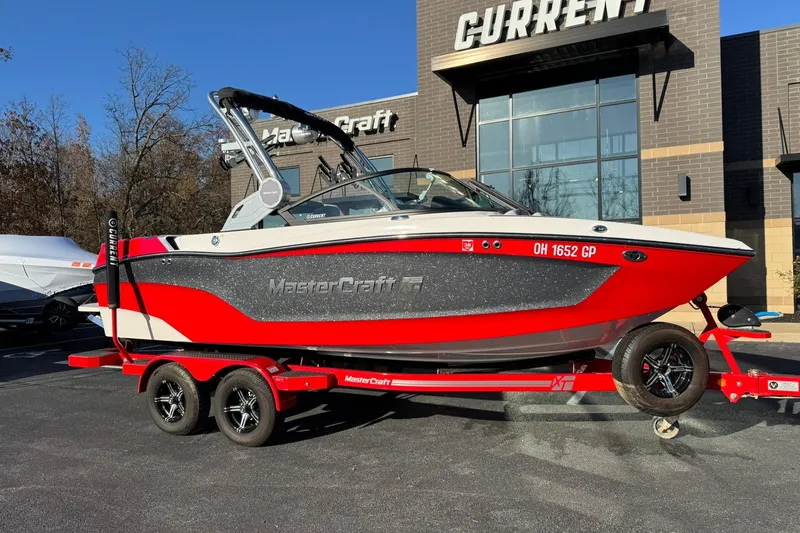 The Image of 2023 MasterCraft XT20 boat in red and gray on a trailer outside a dealership. - 1