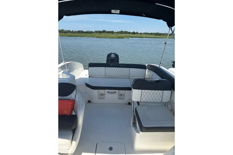Slide: The Image of 2023 Bayliner DX 2200 boat interior with seating, overlooking calm water and greenery. - 7