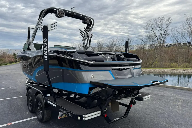 Slide: The Image of 2018 MasterCraft X23 boat on trailer, parked near a lake under cloudy sky. - 5