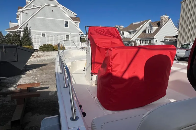 Slide: The Image of 2023 Boston Whaler 170 Montauk boat with red covers, docked near coastal homes. - 7