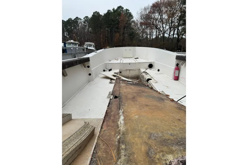 Slide: The Image of 1983 Sea Ox 23 boat interior, showing open deck and visible wear, surrounded by trees. - 4