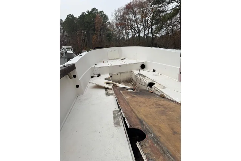 Slide: The Image of 1983 Sea Ox 23 boat interior, showing worn deck and open compartments, surrounded by trees. - 7