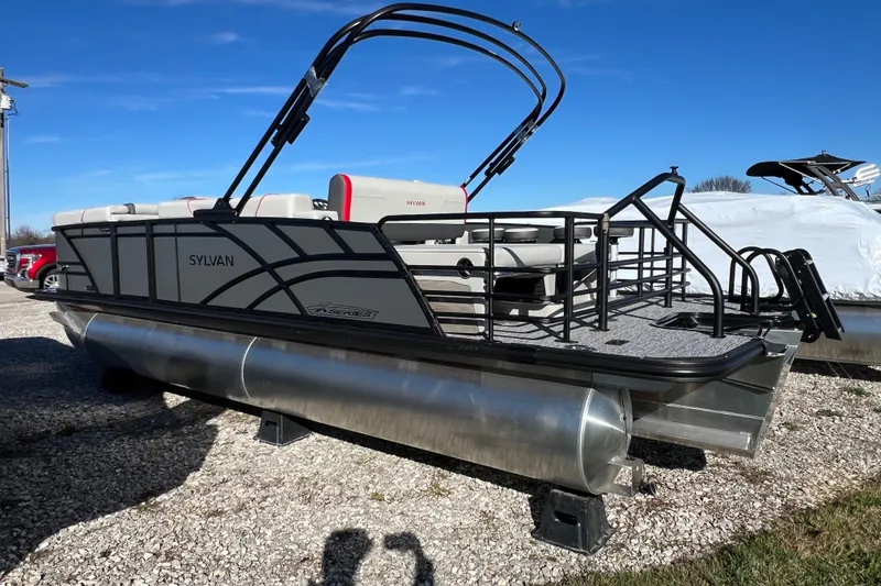 Slide: The Image of 2026 Sylvan X3 DLZ Bar pontoon boat on gravel lot under clear blue sky. - 2