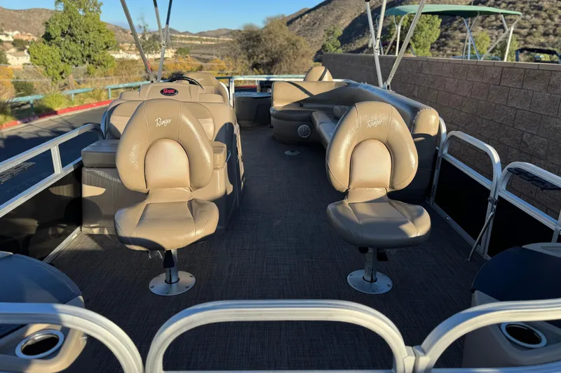 Slide: The Image of 2023 Ranger Reata 200F pontoon boat interior with beige seating and scenic background. - 9