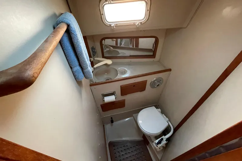 Slide: The Image of Compact bathroom in a 1987 Newport 30-3 sailboat, featuring a toilet, sink, and towel rack. - 18