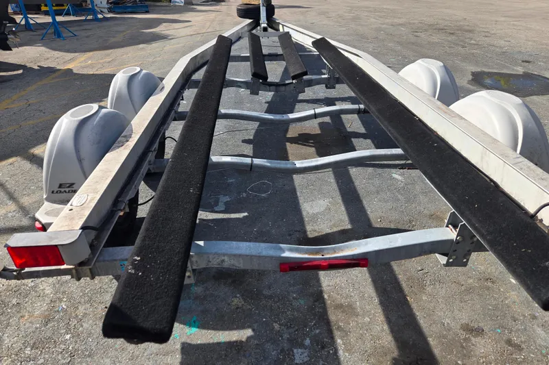 Slide: The Image of 2013 EZ Loader 21-25 trailer on pavement, showcasing dual axles and black carpeted bunks. - 3