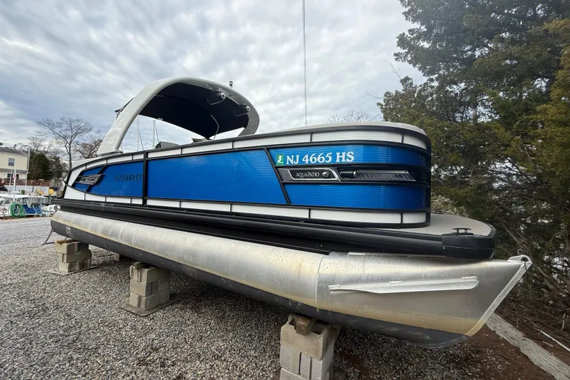 Slide: The Image of 2023 Godfrey AquaPatio 255 ULC pontoon boat on blocks, blue exterior, overcast sky. - 3