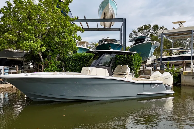Slide: The Image of 2026 Scout 288 LXF boat docked in marina, surrounded by lush greenery and other boats. - 2