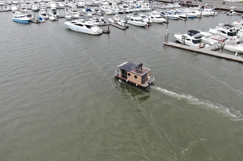 Slide: The Image of Aerial view of 2024 Waterlodge Apart M houseboat navigating a marina with docked boats. - 2