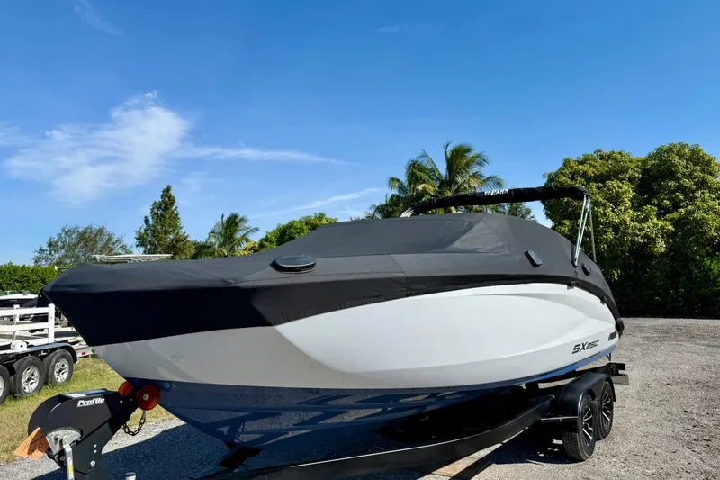 Slide: The Image of 2024 Yamaha Boats SX250 covered on trailer, parked outdoors under clear blue sky. - 29