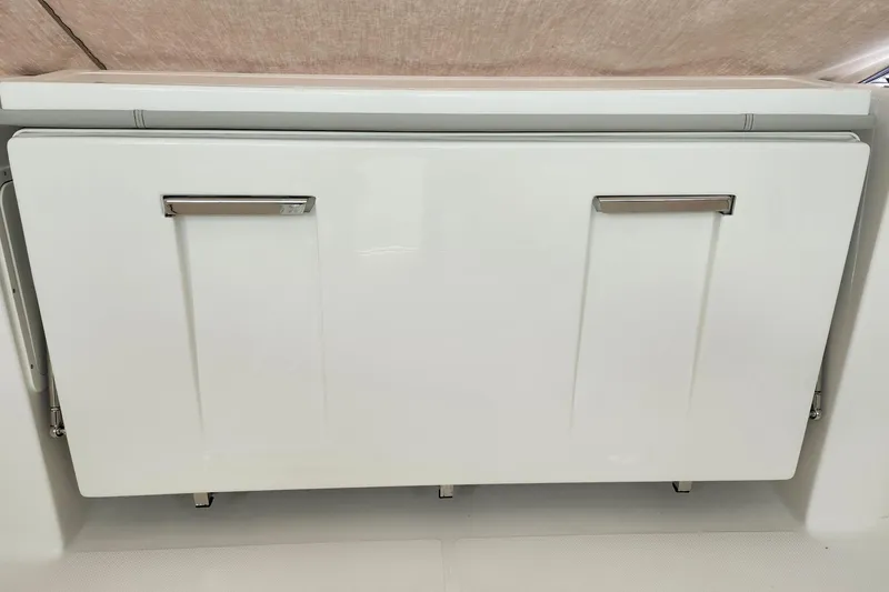 Slide: The Image of 2026 Pursuit DC 326 Dual Console storage compartment with sleek white finish and metal handles. - 29