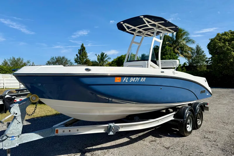 Slide: The Image of 2018 Yamaha Boats 210 FSH Sport on trailer, blue and white, parked outdoors. - 2